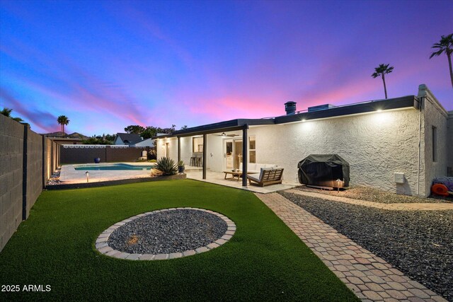 back of house at dusk with ceiling fan, stucco siding, and a patio