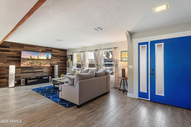 living room featuring wooden walls, an accent wall, wood finished floors, arched walkways, and a fireplace