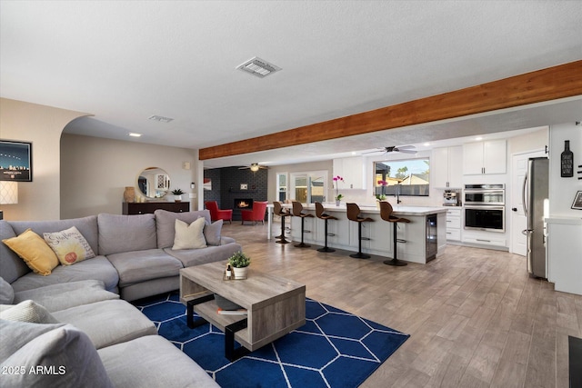 living area featuring ceiling fan, light wood-style flooring, and beam ceiling