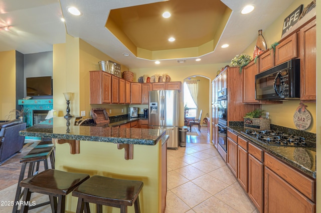 kitchen with a peninsula, light tile patterned flooring, arched walkways, black appliances, and a raised ceiling