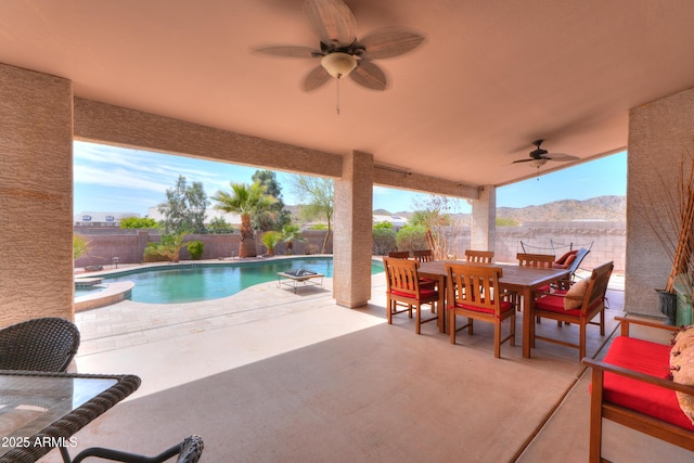 view of patio with a ceiling fan, a pool with connected hot tub, a fenced backyard, a mountain view, and outdoor dining area