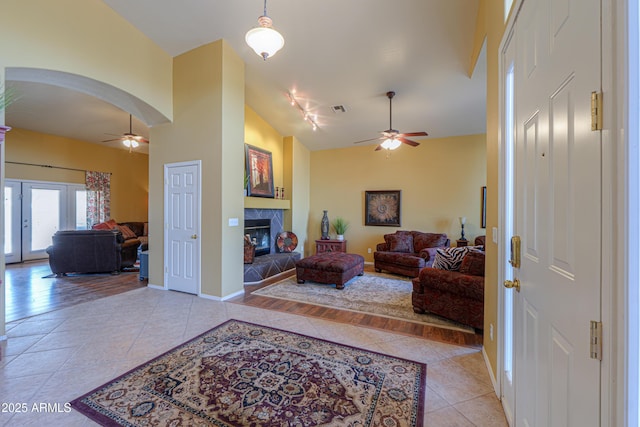 living area with light tile patterned floors, visible vents, arched walkways, ceiling fan, and a tile fireplace