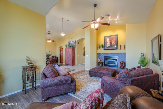 living area featuring a ceiling fan, wood finished floors, arched walkways, a fireplace, and baseboards