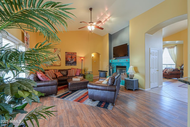 living room with wood finished floors, baseboards, high vaulted ceiling, a fireplace, and arched walkways