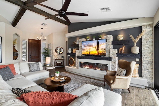 living room with wood-type flooring, lofted ceiling with beams, a stone fireplace, and an inviting chandelier