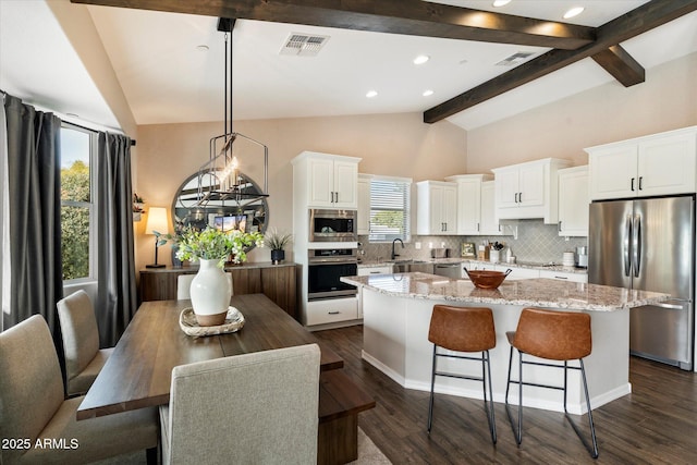 kitchen with appliances with stainless steel finishes, white cabinetry, hanging light fixtures, decorative backsplash, and a kitchen island