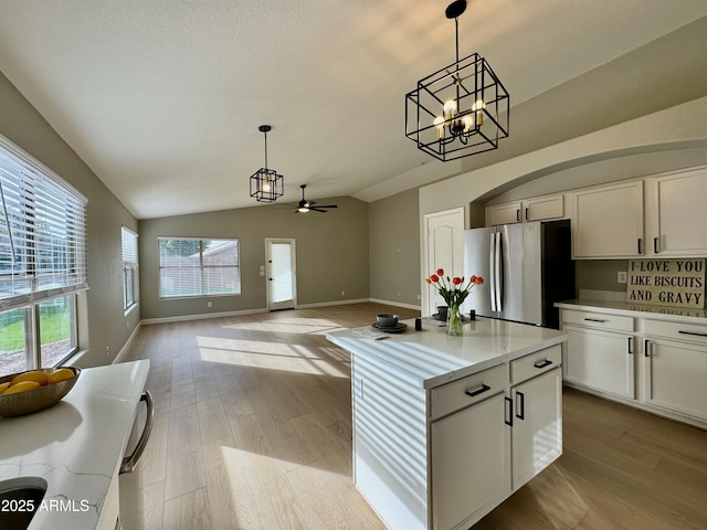 kitchen with decorative light fixtures, stainless steel fridge, lofted ceiling, and white cabinetry