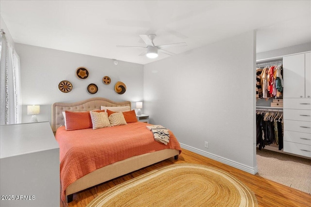 bedroom with a closet, a spacious closet, baseboards, and wood finished floors