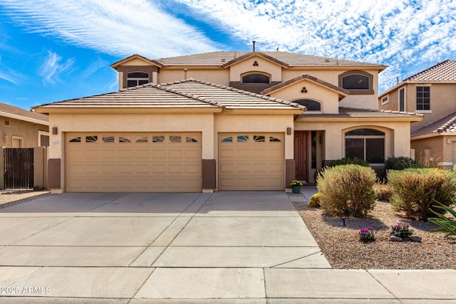 mediterranean / spanish-style home featuring a garage, driveway, a tiled roof, fence, and stucco siding