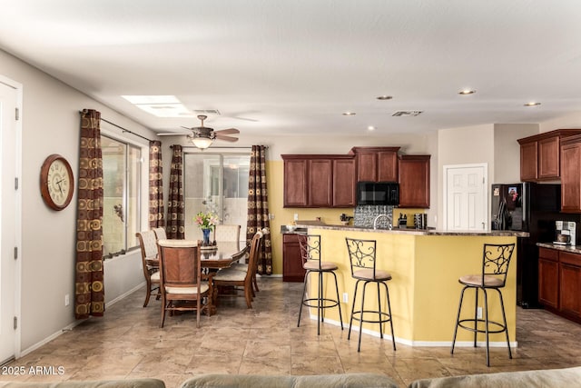 kitchen with a kitchen island with sink, recessed lighting, visible vents, black appliances, and a kitchen bar