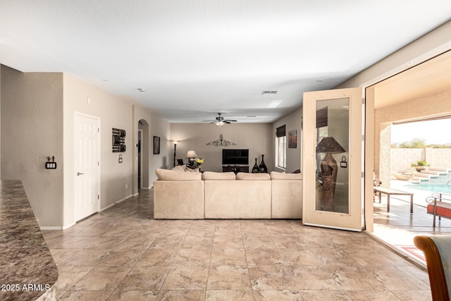 living room featuring a ceiling fan, arched walkways, visible vents, and baseboards