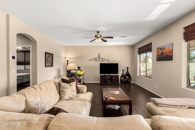 living room featuring visible vents, baseboards, arched walkways, ceiling fan, and dark wood-style flooring