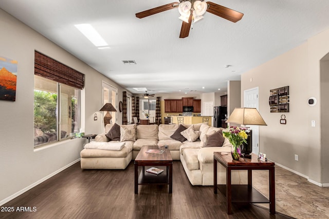 living room with dark wood-style flooring, a skylight, visible vents, and baseboards