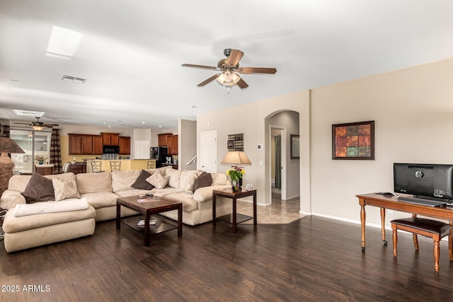 living room with arched walkways, dark wood-style flooring, visible vents, a ceiling fan, and baseboards