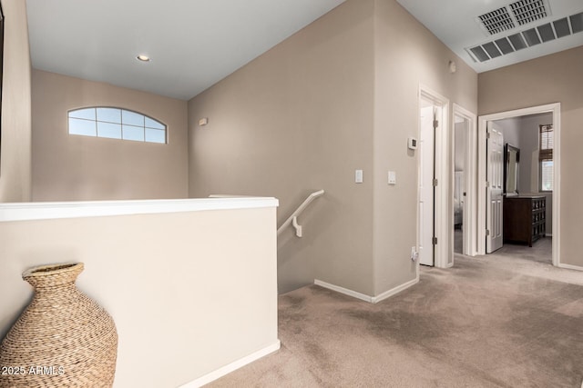 hall with carpet floors, baseboards, visible vents, and an upstairs landing