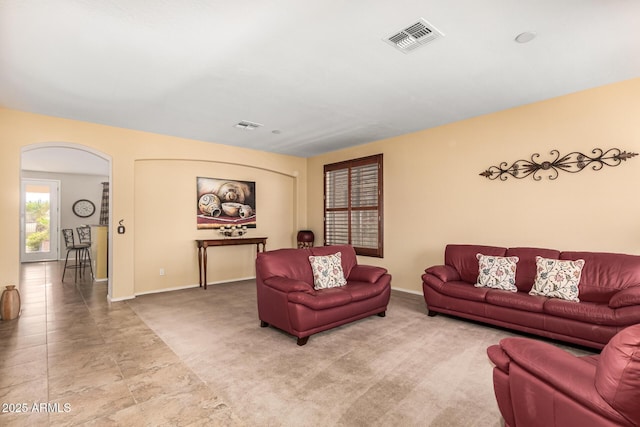 carpeted living area with arched walkways, visible vents, and baseboards