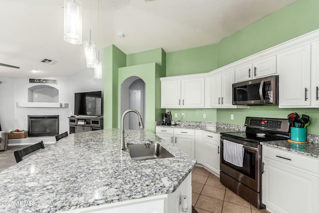 kitchen with a glass covered fireplace, appliances with stainless steel finishes, open floor plan, a kitchen island with sink, and a sink