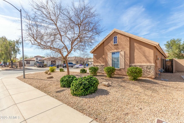 view of side of property featuring stone siding, fence, a residential view, and stucco siding