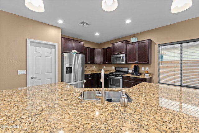 kitchen featuring dark brown cabinetry, sink, light stone counters, decorative light fixtures, and stainless steel appliances