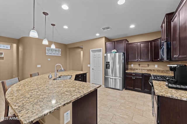 kitchen featuring sink, light stone counters, hanging light fixtures, an island with sink, and stainless steel appliances