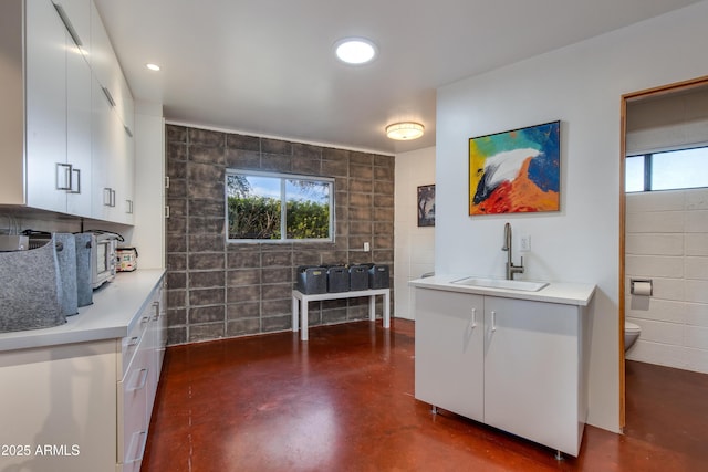 kitchen with white cabinetry, plenty of natural light, sink, and tile walls