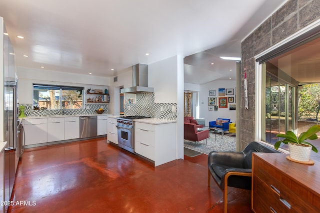 kitchen with wall chimney range hood, plenty of natural light, white cabinets, and appliances with stainless steel finishes