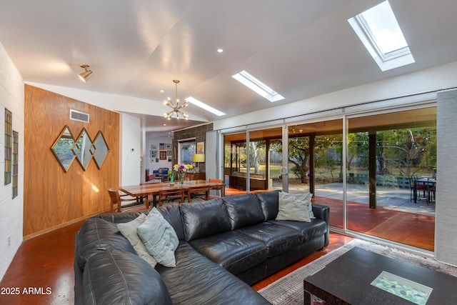 living room with wooden walls, a chandelier, and vaulted ceiling with skylight