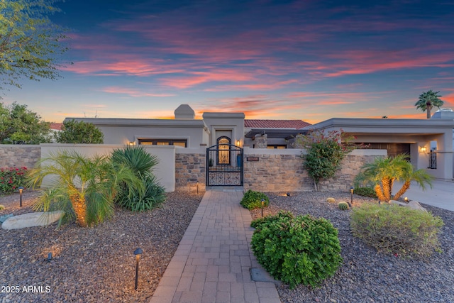 view of front of property with a fenced front yard, an attached garage, a gate, and stucco siding