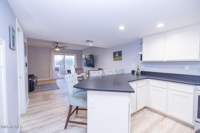 kitchen featuring white cabinetry, light wood-type flooring, a kitchen breakfast bar, kitchen peninsula, and ceiling fan