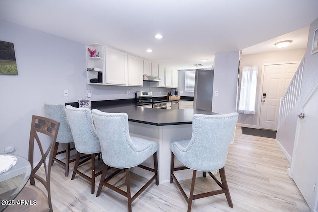 kitchen featuring white cabinetry, light hardwood / wood-style flooring, a kitchen breakfast bar, kitchen peninsula, and stainless steel appliances