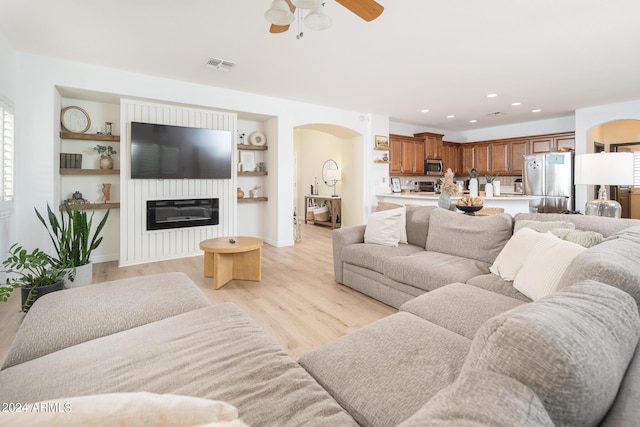 living room featuring light wood-type flooring, ceiling fan, and built in shelves