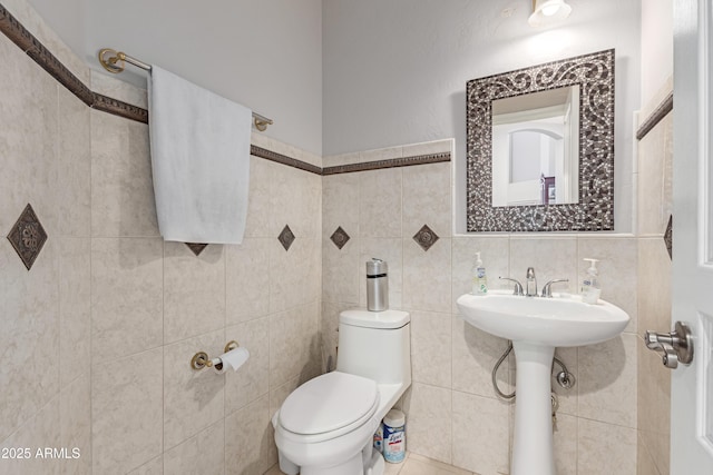 half bath with toilet, a sink, and tile walls