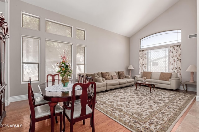 living room featuring baseboards, visible vents, high vaulted ceiling, and light wood-style flooring
