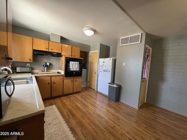 2564 Mockingbird Dr, Sierra Vista, AZ 85635 - kitchen with black appliances, tile countertops, under cabinet range hood, a sink, and wood finished floors