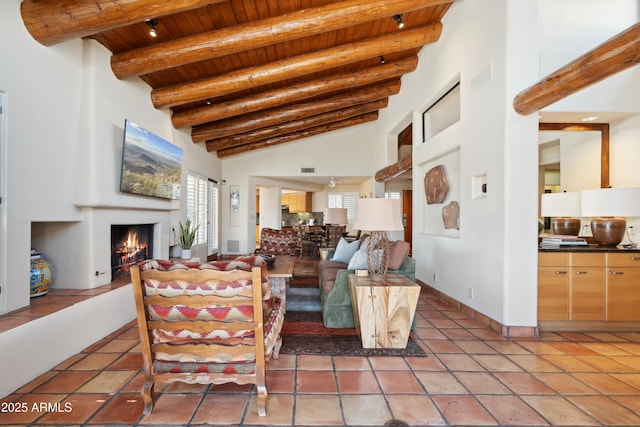 living area featuring light tile patterned floors, high vaulted ceiling, wood ceiling, a lit fireplace, and beam ceiling