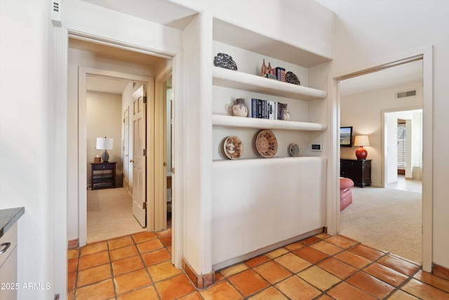 hallway with light carpet, light tile patterned floors, visible vents, and built in features