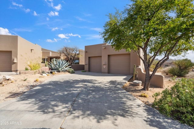 pueblo revival-style home featuring a garage, concrete driveway, and stucco siding