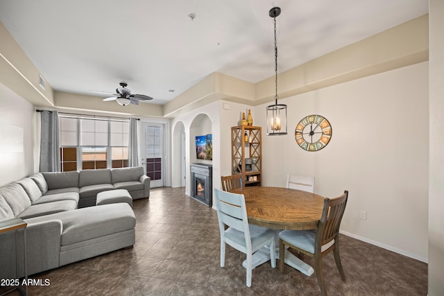 dining room featuring visible vents, baseboards, a warm lit fireplace, and a ceiling fan