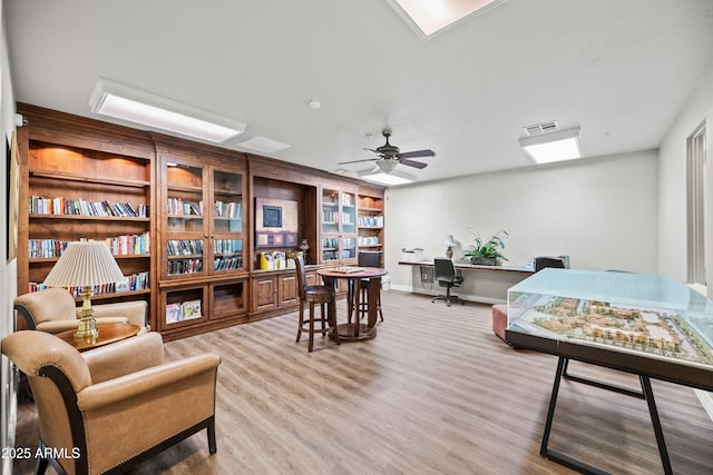 interior space with a ceiling fan, wood finished floors, visible vents, built in study area, and baseboards