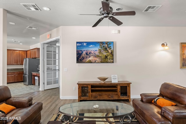 living area featuring light wood-style flooring, a ceiling fan, visible vents, and baseboards