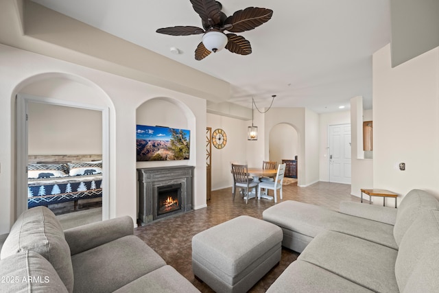 living room with a lit fireplace, baseboards, and a ceiling fan