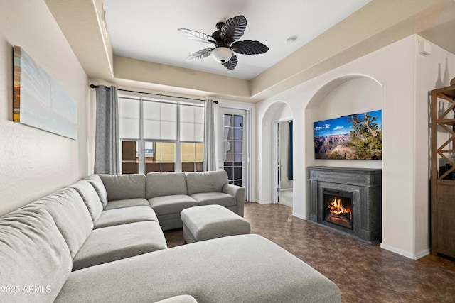 living area with baseboards, a warm lit fireplace, and a ceiling fan