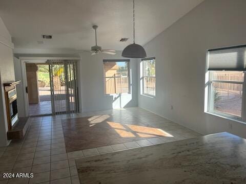 empty room featuring a fireplace with raised hearth, ceiling fan, high vaulted ceiling, dark tile patterned flooring, and visible vents