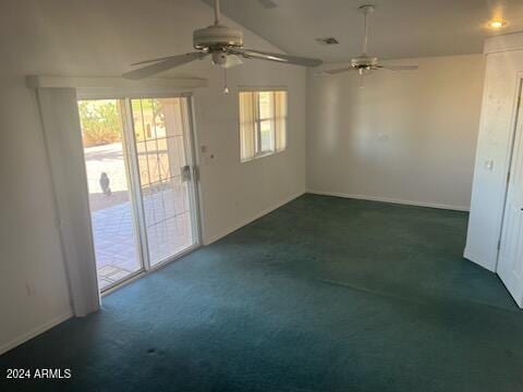 empty room featuring vaulted ceiling, dark colored carpet, and a wealth of natural light