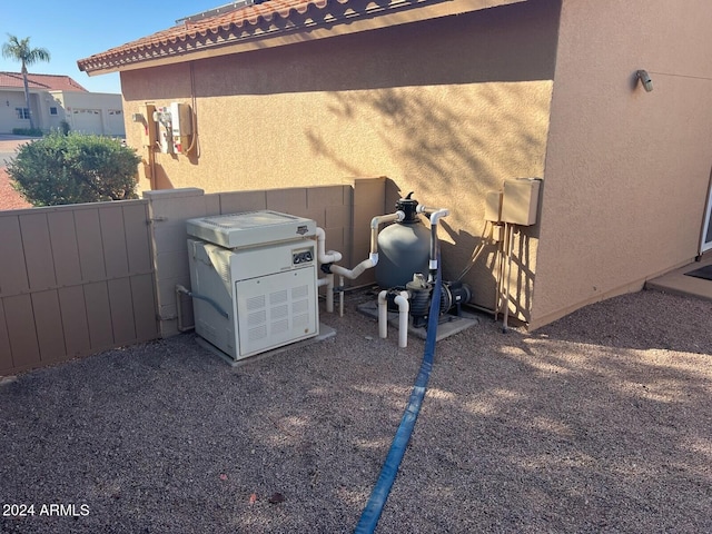 exterior details featuring a power unit, fence, a gate, stucco siding, and pump