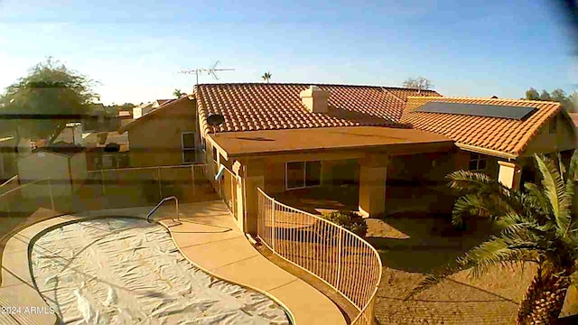 back of house with a tile roof, roof mounted solar panels, and a patio