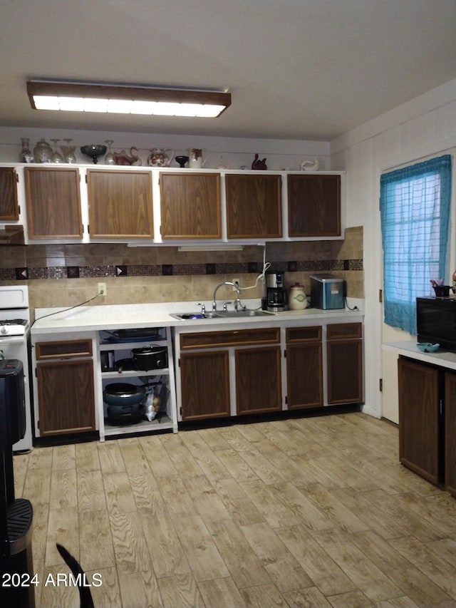 kitchen with light wood-type flooring, tasteful backsplash, dark brown cabinets, white range, and sink