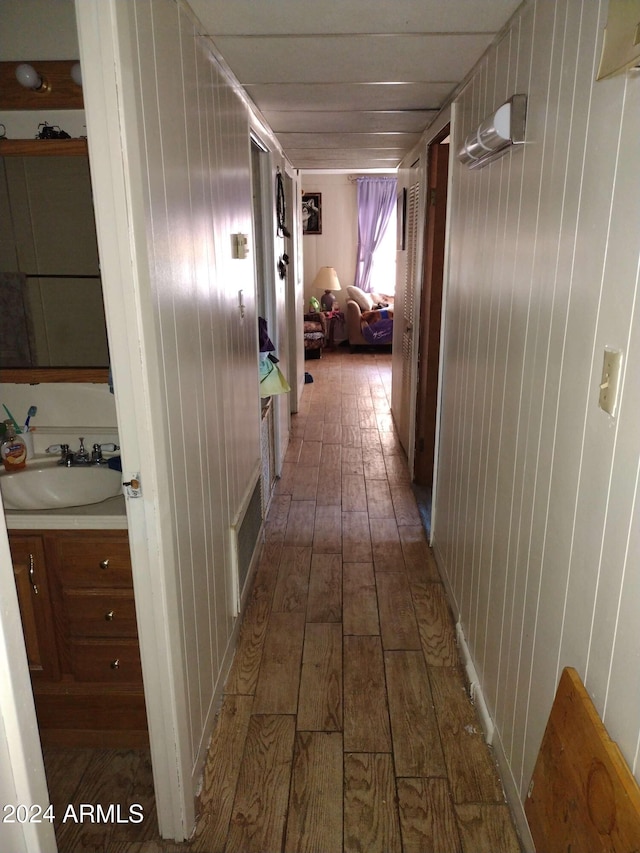 corridor with wooden walls, dark wood-type flooring, and sink