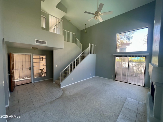 unfurnished living room with ceiling fan, a towering ceiling, and carpet