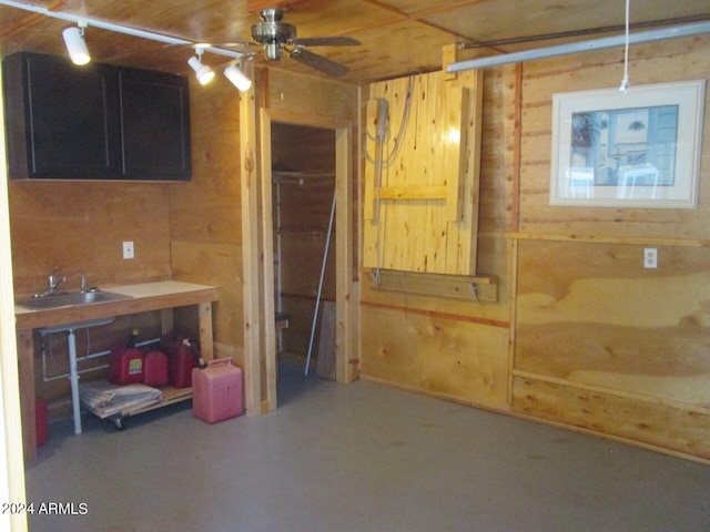 basement featuring ceiling fan, wood walls, and a sink